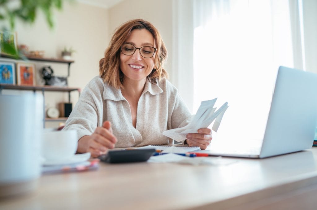 A woman looking at finances and her laptop and she is smiling